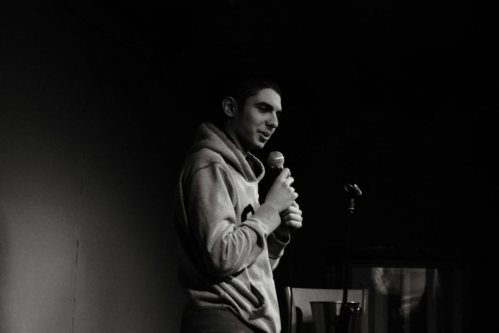 Black and white photo of a comic holding a microphone on a dark stage