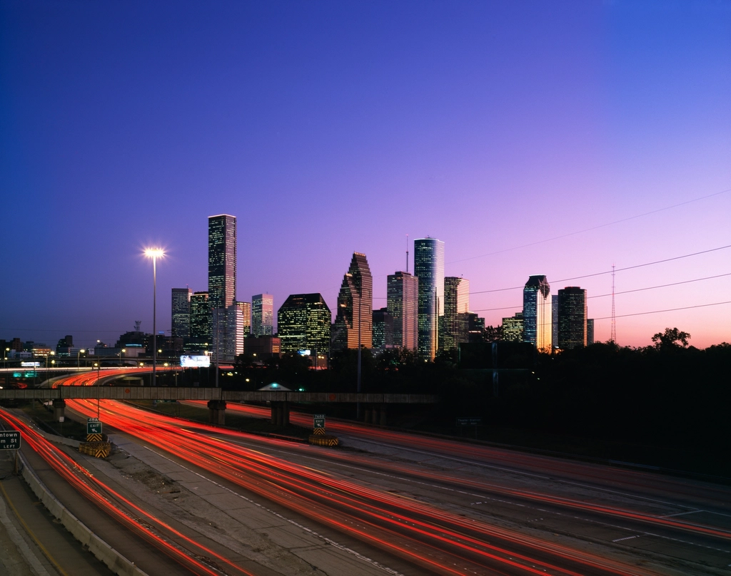 Downtown Houston skyline at dusk behind a freeway streaked with car light trails
