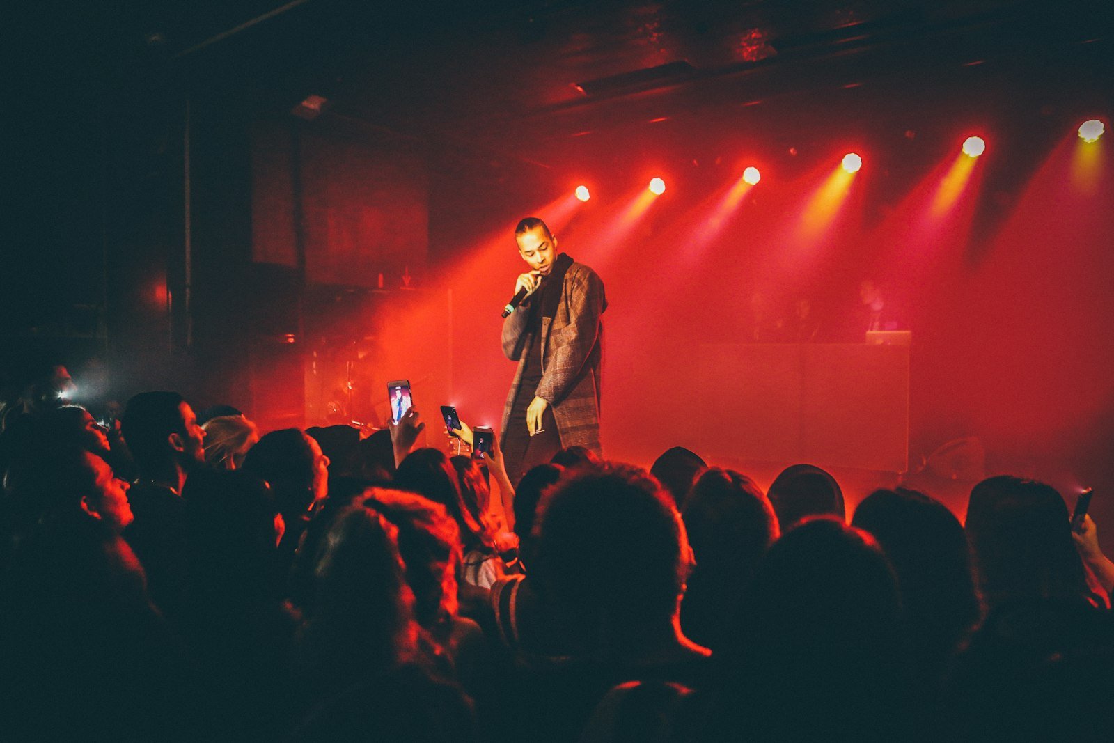 Comedian holding a microphone on stage under red lights in front of a standing crowd