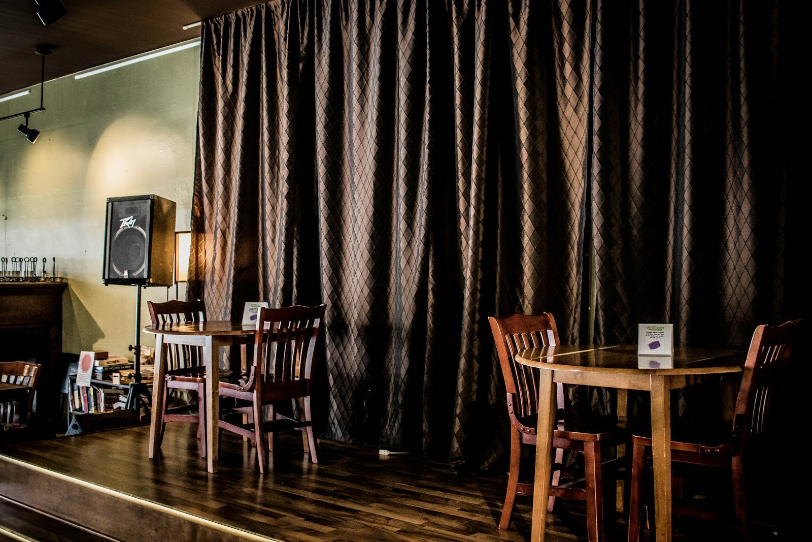 Small bar stage corner with a curtain backdrop, speaker, and wooden tables and chairs
