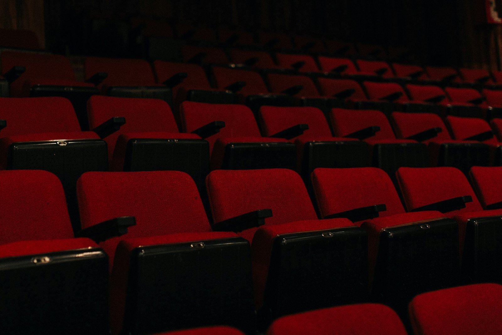 Rows of empty red velvet theatre seats fading into a dark room