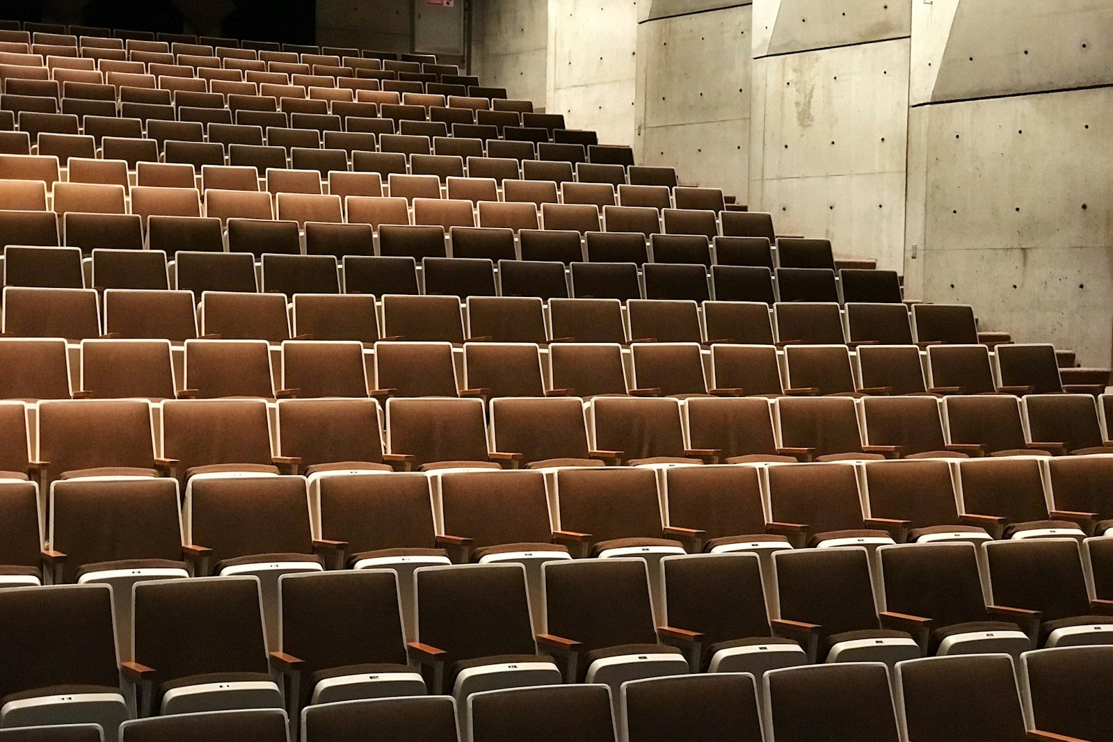 Rows of empty fold-down auditorium seats climbing away from the stage under low warm light