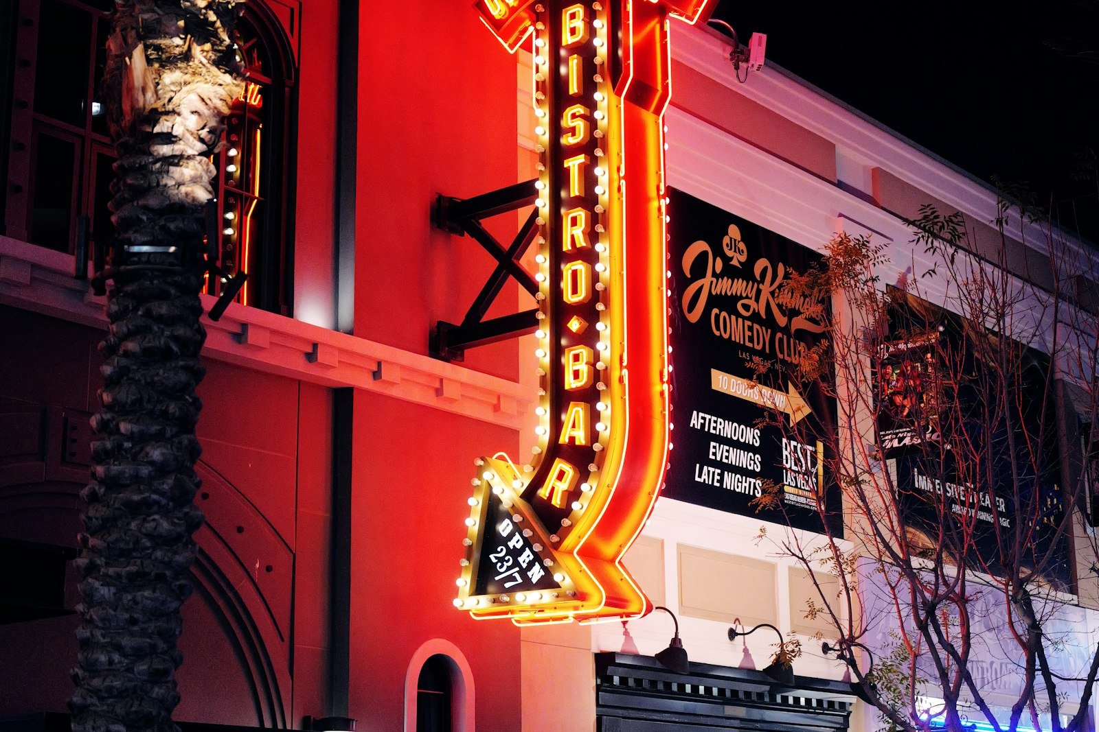 Neon bistro bar sign beside a comedy club billboard listing afternoon, evening and late night shows