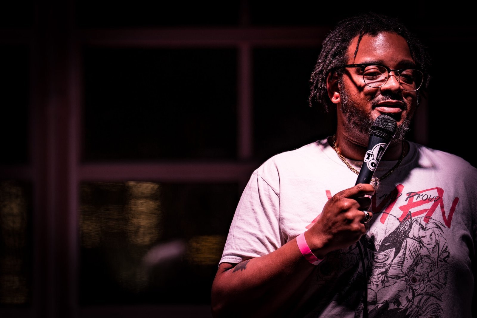 Comedian holding a microphone in a dark room, shot on a Sony a7 IV from the back of the venue with the face cleanly exposed