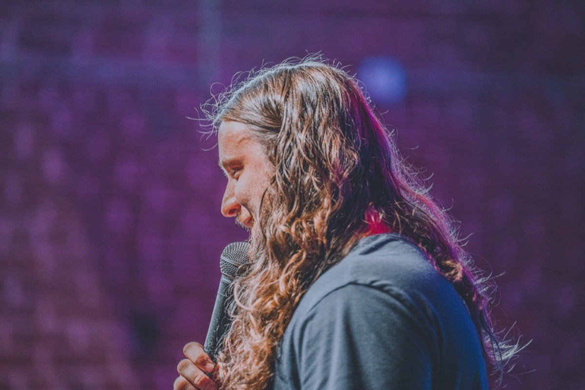 Side profile of a comedian at the microphone under purple stage light, shot on a mirrorless camera in low light
