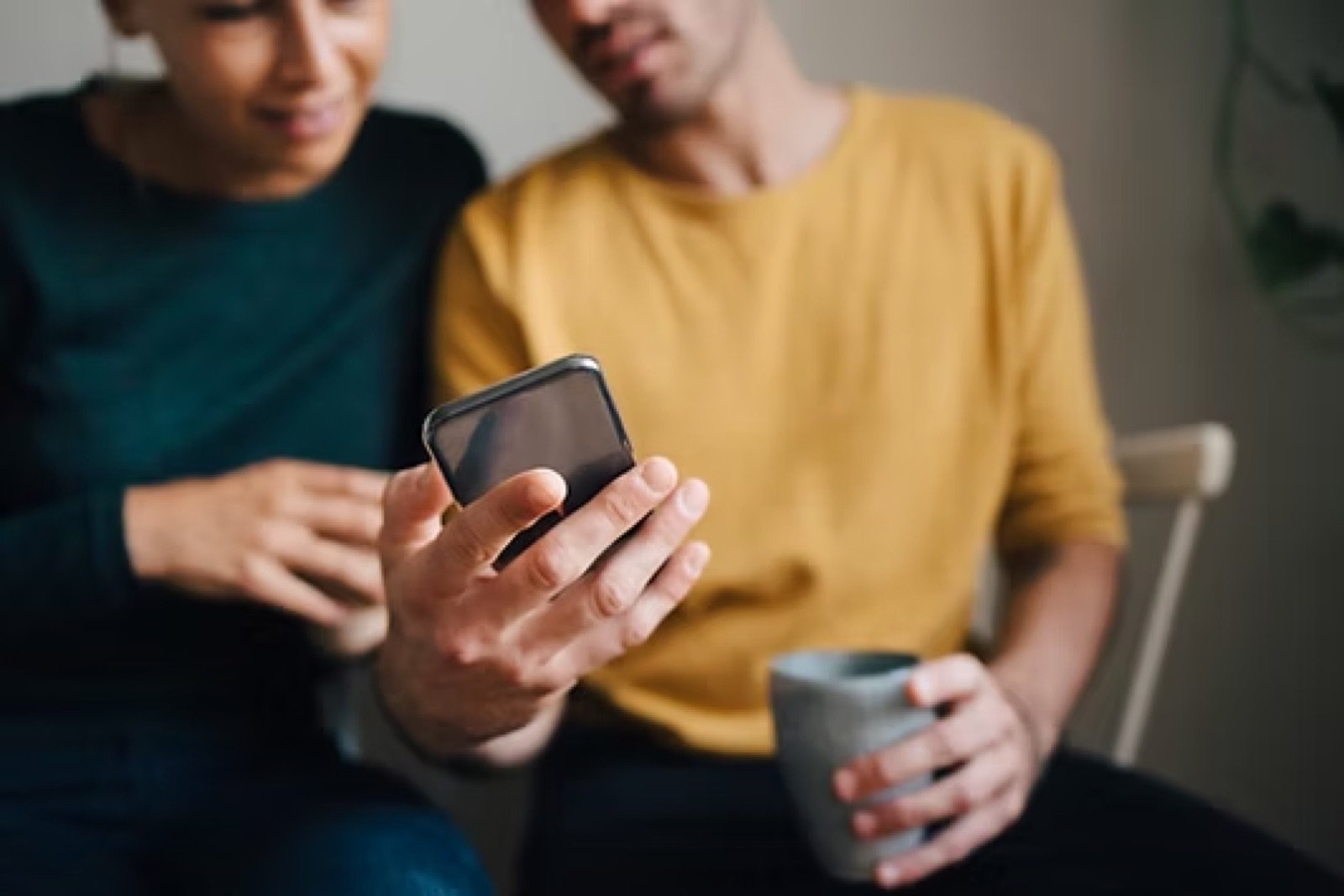 Two people on a couch watching a clip on a phone, one holding a coffee mug