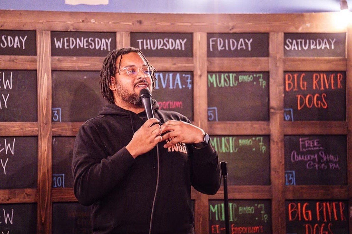 Comedian with a handheld microphone in front of a chalkboard events wall