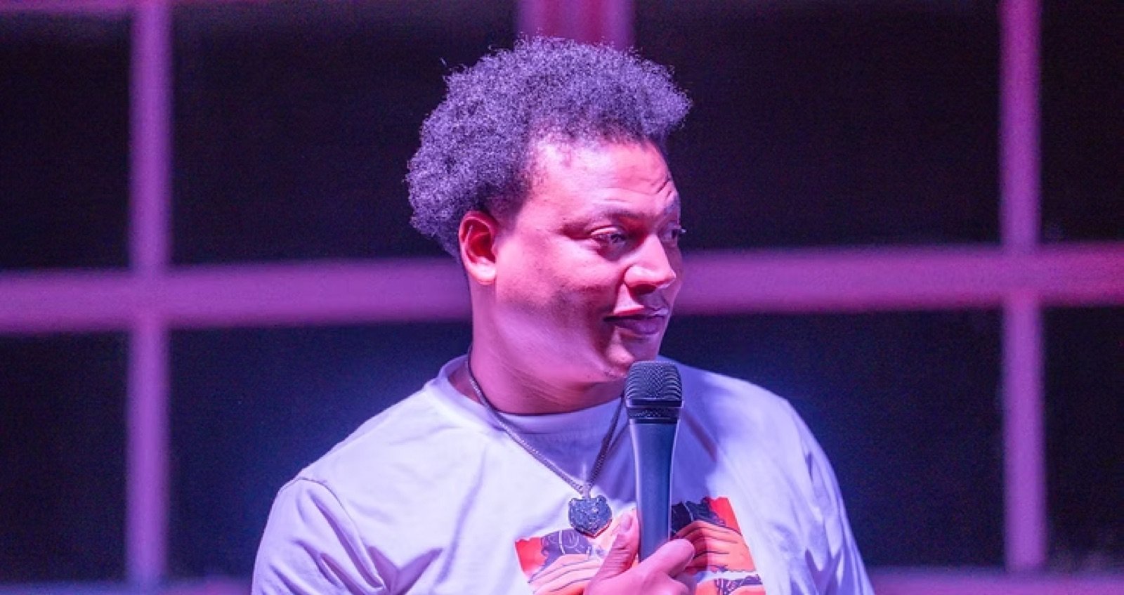 Comedian in purple stage lighting holding a microphone