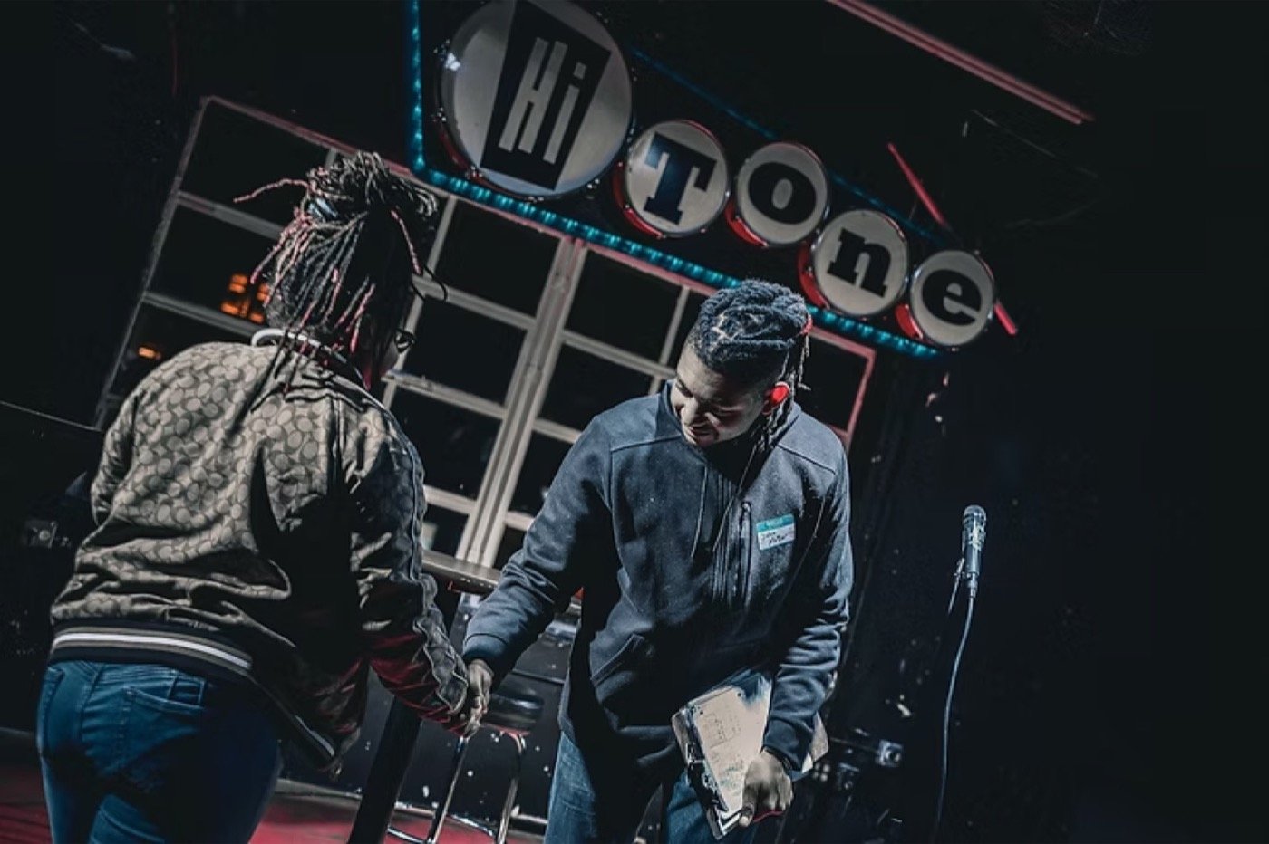 Two comedians shaking hands on stage under the Hi Tone club sign