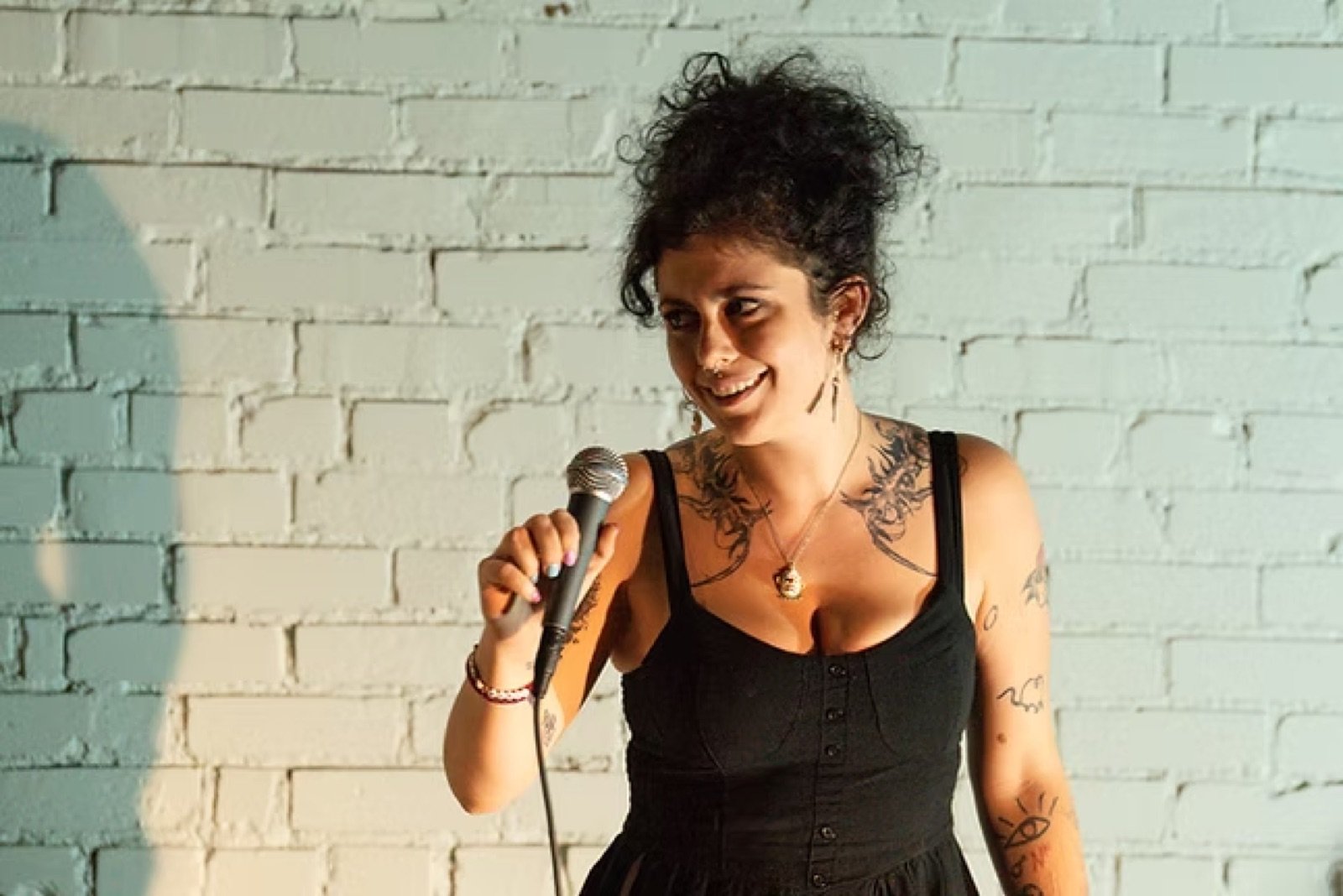 Comedian smiling with a wired microphone against a white brick wall