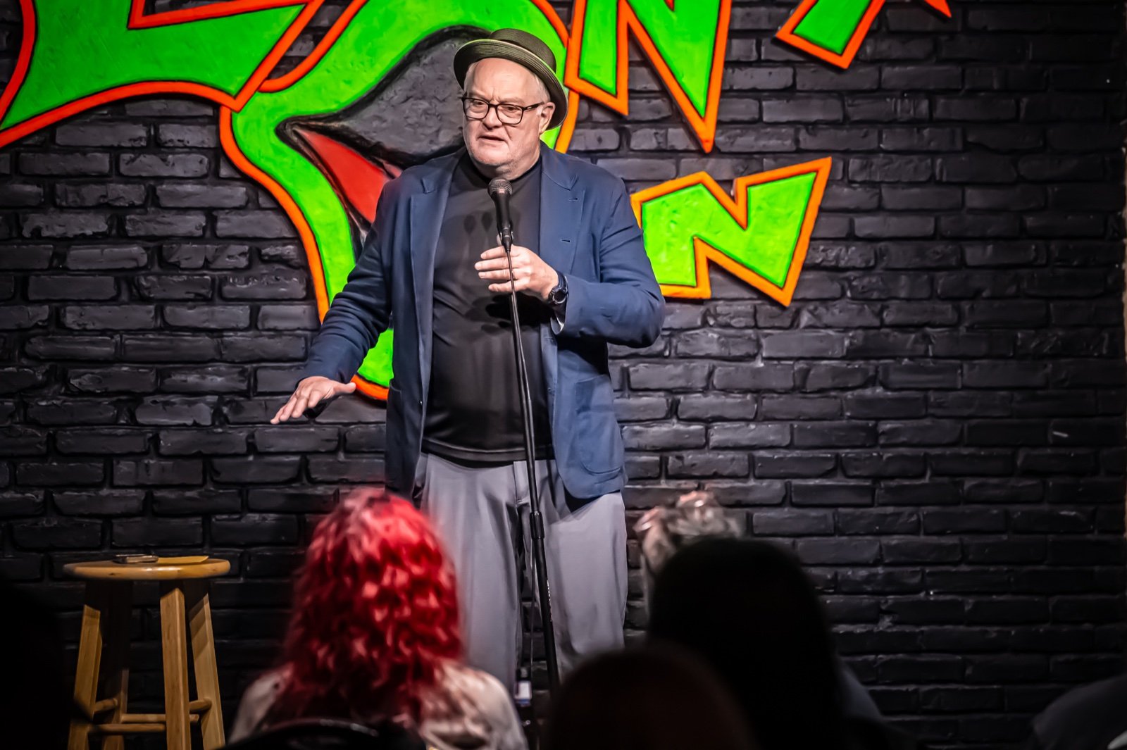 Comedian on stage against a painted brick wall under stage lights