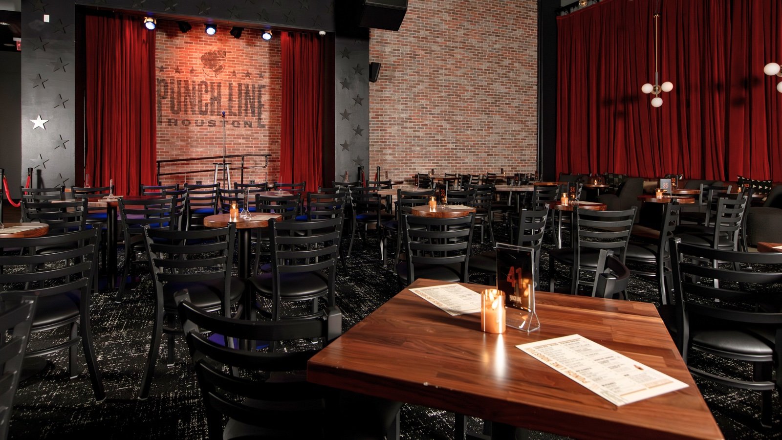 Punch Line Houston showroom with red stage curtains, a brick wall, and candlelit tables